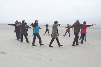 Menschen gehen im Kreis am Strand, ein Tau haltend